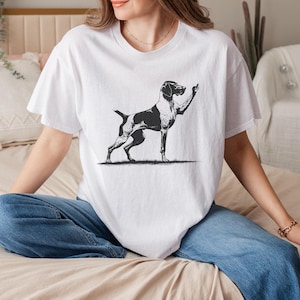May include: A white t-shirt featuring a black and white illustration of a dog giving the middle finger.