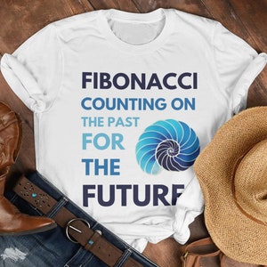 Könnte beinhalten: Weißes T-Shirt mit einer blauen und weißen Spiralgrafik und dem Text "Fibonacci Counting on the Past for the Future". Das Shirt liegt auf einer Holzoberfläche mit einem Paar braunen Cowboystiefeln, einer braunen Ledertasche, einem braunen Hut und einer Sonnenbrille.