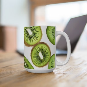 May include: White ceramic mug with a design of green kiwi fruit slices. The mug has a large handle.
