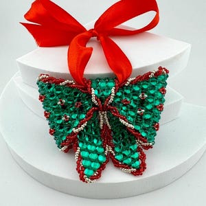 Könnte beinhalten: Ein grüner und roter Weihnachtsbaumschmuck in Form einer Schleife mit einem roten Band.