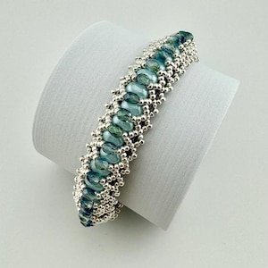 Könnte beinhalten: Ein silbernes und blaues Armband mit geometrischem Muster. Das Armband besteht aus kleinen silbernen Perlen und größeren, ovalen blauen Perlen.