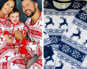 May include: Matching pajamas featuring a white base with a repeating pattern of dark blue reindeer and snowflakes. The set includes a long-sleeved top with a crew neckline and coordinating pants, showcasing a consistent festive geometric print.