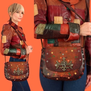 May include: A brown leather crossbody bag with a flap closure, decorated with colourful floral embroidery and a decorative metal clasp. The bag is worn with a patchwork leather jacket in shades of brown, red, green, and tan.