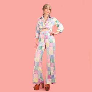 May include: A pastel patchwork two-piece outfit. The set includes a button-down shirt tied at the waist and wide-leg trousers. The outfit is made of squares of pink, yellow, blue, and green fabric. The model is wearing platform heels.