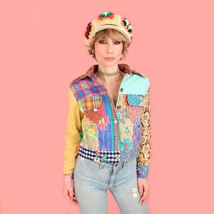 May include: A multicolored patchwork jacket featuring various fabric patterns including plaid, floral, and gingham, paired with light blue denim jeans and a crocheted granny square hat with a brim, showcasing a vibrant mix of textures and colors.