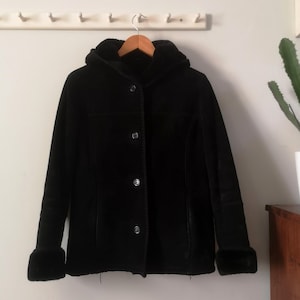 May include: A black hooded jacket with a fur trim around the hood and cuffs. The jacket has a button closure and a few pockets.