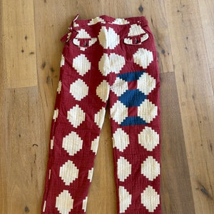 May include: Red quilted pants with a white polka dot pattern. The pants have a blue and white patchwork design on one leg.