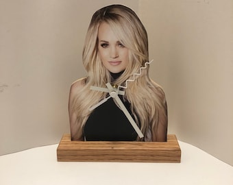 May include: A wooden clock with a picture of a woman with long blonde hair. The clock face is white with black hands.
