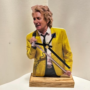 May include: A yellow and black clock featuring a musician holding a microphone. The clock is on a wooden base.