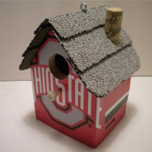 May include: A red and grey birdhouse with a shingled roof and the words "Ohio State" on the front. The birdhouse has a small opening for birds to enter.
