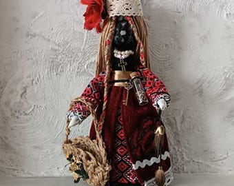 May include: A handmade doll with a black face, wearing a red and black patterned dress and a floral headpiece. The doll holds a woven basket and has long, braided hair. A small vial with a key hangs around its neck.