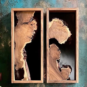 May include: Two wooden frames with black resin inserts, showcasing a natural wood grain pattern. The frames are mounted on a textured teal and brown wall.