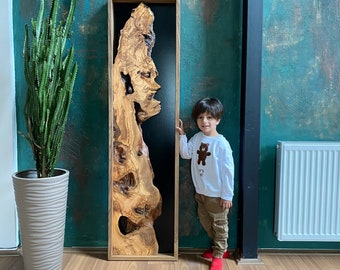May include: A wooden wall art piece with a natural wood grain pattern and a black background. The art is framed in a dark wood frame and is hanging on a teal wall. A young person is standing next to the art, looking at the camera.