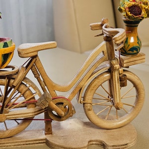 Könnte beinhalten: Eine Holzfigur eines Fahrrads mit einem Wassermelonenkorb auf dem Gepäckträger und einer Vase mit einer Sonnenblume am Lenker.