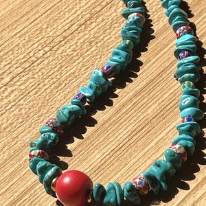 May include: A turquoise and red beaded necklace with a large red bead in the center. The necklace is made of irregular shaped turquoise beads with small red, blue, and white beads interspersed throughout.