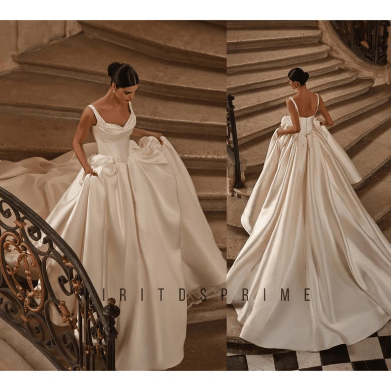K&ouml;nnte beinhalten: Eine Braut in einem wei&szlig;en Satin-Hochzeitskleid mit herzf&ouml;rmigem Ausschnitt und einem flie&szlig;enden Rock. Das Kleid ist mit zarten Perlen verziert und die Braut geht eine gro&szlig;e Treppe hinunter.