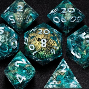 May include: A set of seven polyhedral dice with a teal and gold color scheme. The dice are transparent, with a swirling teal interior and gold accents. Each die has white numbering.