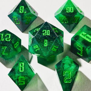 Puede incluir: Juego de siete dados poliédricos verdes, ideales para juegos de rol. Cada dado presenta una forma única y números verdes brillantes. El conjunto incluye un d4, d6, d8, d10, d12, d20 y un dado de porcentaje, con un efecto veteado.