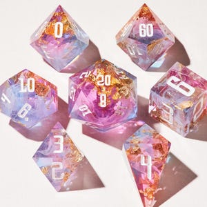 May include: Set of seven polyhedral dice with a clear, iridescent appearance. Each die is filled with gold flakes and swirls of pink, purple, and blue. White numbers are visible on each face. Ideal for tabletop games.