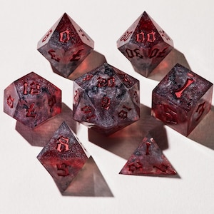 May include: Set of seven polyhedral dice in shades of red and gray. The dice are transparent with red numbering and a speckled interior. The set includes a d4, d6, d8, d10, d12, d20, and a percentile die, perfect for tabletop gaming.