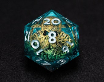 May include: A teal and gold twenty-sided die with white numbering. The die is transparent, revealing a gold-colored creature inside. The numbers are in a clean, sans-serif font. This unique die is perfect for tabletop gaming.
