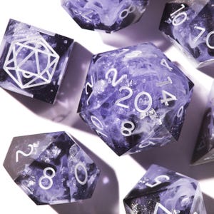 May include: A set of polyhedral dice featuring a translucent purple and black resin base with swirling white smoke patterns and embedded silver foil flakes. The dice have crisp white engraved numbers and a geometric logo on the d20 face.