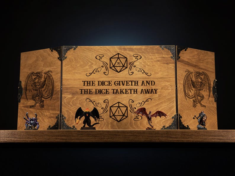 K&ouml;nnte beinhalten: Holz-Tischspiel-Sichtschutz mit eingravierten W&uuml;rfeln und Drachendesigns. Auf der Mittelplatte steht "THE DICE GIVETH AND THE DICE TAKETH AWAY." Enth&auml;lt Miniaturfiguren auf einem Holzregal.