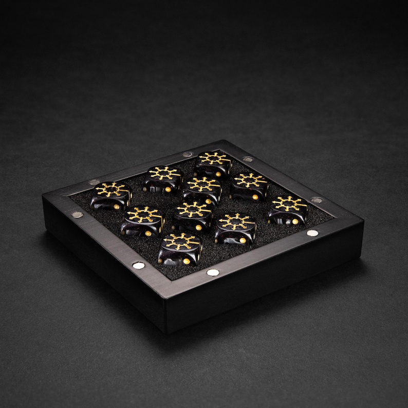 May include: A black display case holds ten black and gold decorative objects. Each object has a gold wheel design on top. The case is square with a black frame and a dark interior. The objects are evenly spaced within the case.
