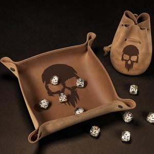 May include: A brown leather dice tray and matching drawstring bag, both featuring a skull design. Several speckled dice are scattered around the tray. The set is designed for tabletop gaming.