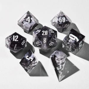 May include: A collection of seven polyhedral dice, ideal for role-playing games. The dice feature a black and white marbled design with white numbering. They are displayed on a white surface.
