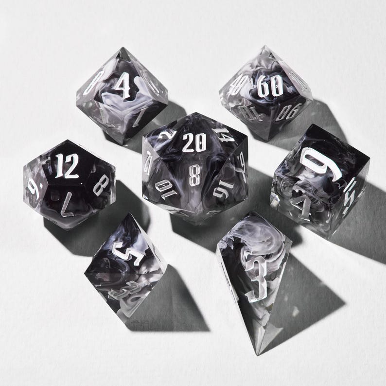 May include: A collection of seven polyhedral dice, ideal for role-playing games. The dice feature a black and white marbled design with white numbering. They are displayed on a white surface.