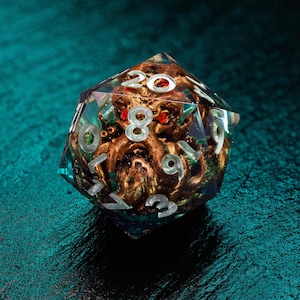 May include: A clear, multi-sided dice with a gold and green creature inside. The numbers 1 through 20 are visible on the faces of the dice.