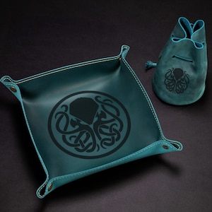 Op de afbeelding: Teal leren dienblad en trekkoordzakje set. De lade heeft een vierkante vorm met afgeronde hoeken en een zwart octopusontwerp. De tas heeft een bijpassend octopusontwerp. De set is gemaakt van leer.