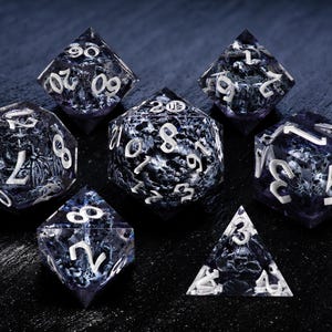 K&ouml;nnte beinhalten: Set aus sieben polyedrischen W&uuml;rfeln mit einem dunkelblauen und wei&szlig;en Marmormuster. Jeder W&uuml;rfel hat wei&szlig;e Zahlen. Die W&uuml;rfel sind f&uuml;r Tabletop-Rollenspiele konzipiert und werden auf einer dunklen Oberfl&auml;che pr&auml;sentiert.