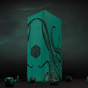 May include: A teal dice box with black tentacles and geometric designs. Several green and gold dice are scattered in front of the box. The box is rectangular and stands upright against a dark background.
