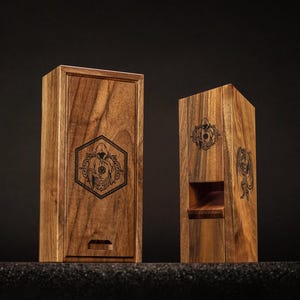May include: Two wooden boxes with engraved designs. One is rectangular with a sliding lid, the other is a tall, open-front box. Both are made of wood with a natural grain and feature a dark, detailed graphic.