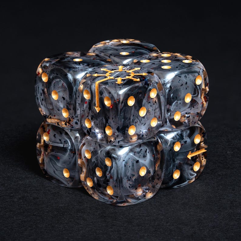 May include: Six black and gray marbled dice with gold-colored pips and symbols are stacked together. The dice have a swirling pattern and are arranged in a cube shape. The dice are for a tabletop game.