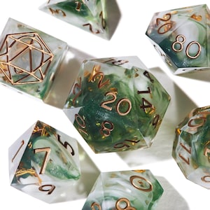 May include: A set of seven polyhedral dice made of clear resin with swirling green and white inclusions and gold-coloured flakes. The numbers are engraved in a metallic copper finish. The d20 die is centred, surrounded by other dice shapes.