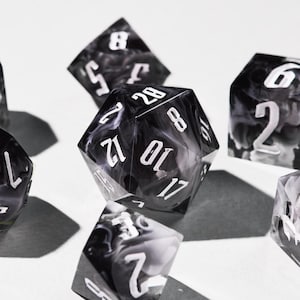 May include: Close-up of several polyhedral dice with white numbering on a black and white marbled design. The dice are in various shapes, including a 20-sided die. The dice are used for tabletop games.