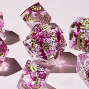 Peut inclure: Ensemble de dés en résine transparente avec un motif floral violet et argenté. Les dés ont des chiffres verts, parfaits pour les jeux de rôle sur table.