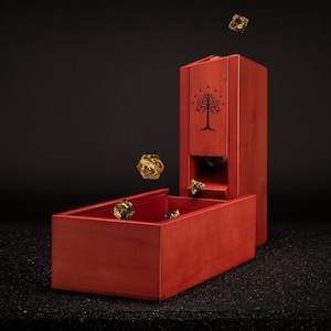 May include: A red wooden dice tower and tray set with a tree design. Several gold-coloured dice are shown in the air and inside the tray. The tower has a slot for the dice to roll through.
