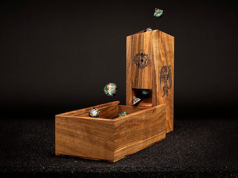 May include: A wooden dice tower and tray set. The tower has engraved designs and a slot for dice to roll into the tray. Several colourful dice are in the tray and falling from the tower. The set is made of a light brown wood.