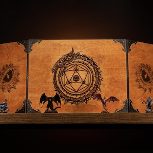 Puede incluir: Un tablero de juego de madera de tres paneles con un diseño de dragón y pentagrama. El tablero está decorado con detalles de metal negro y presenta una pequeña figura de dragón en el panel frontal.