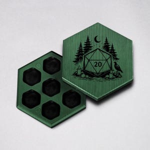 以下が含まれることがあります： 森とD20のデザインが施された緑色の木製サイコロボックス。六角形のボックスを開くと、6つのサイコロコンパートメントが現れます。蓋には、木、月、鳥、数字20のD20サイコロの詳細なイラストが描かれています。
