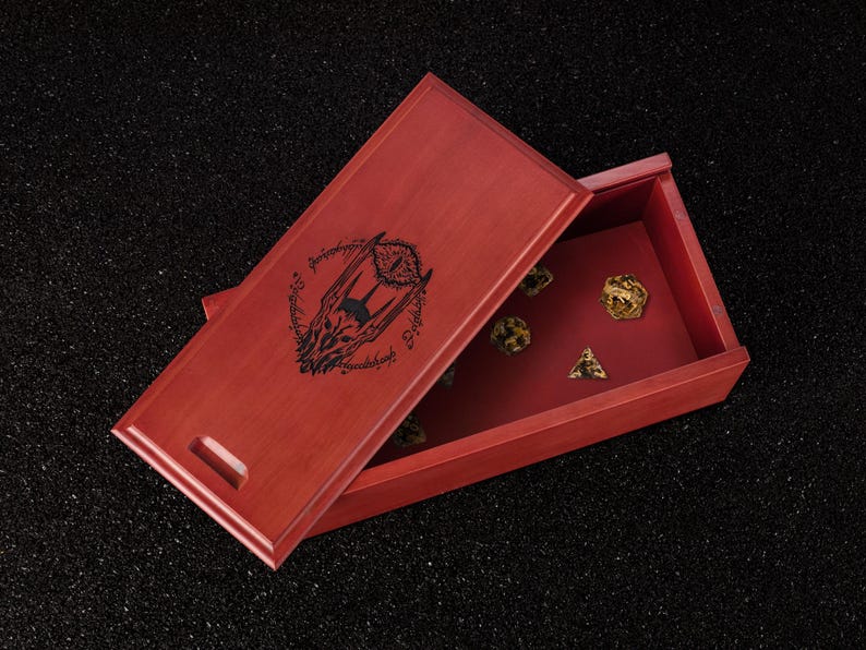May include: A red wooden dice box with a hinged lid, featuring a black graphic design and text. The box is open, revealing several dice in various shapes and colors. The dice box is on a black surface.