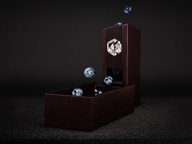May include: A dark wood dice tower and tray set with a geometric design. Several blue and white dice are shown in the tray, falling from the tower, and in mid-air. The tower has a decorative emblem on the front.