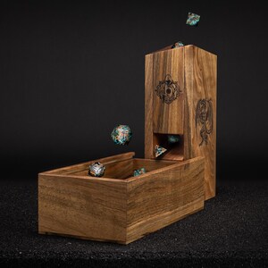 May include: A wooden dice tower and tray set. The tower has engraved designs and a slot for dice to roll into the tray. Several colorful dice are in the air and in the tray. The set is made of a warm-toned wood.
