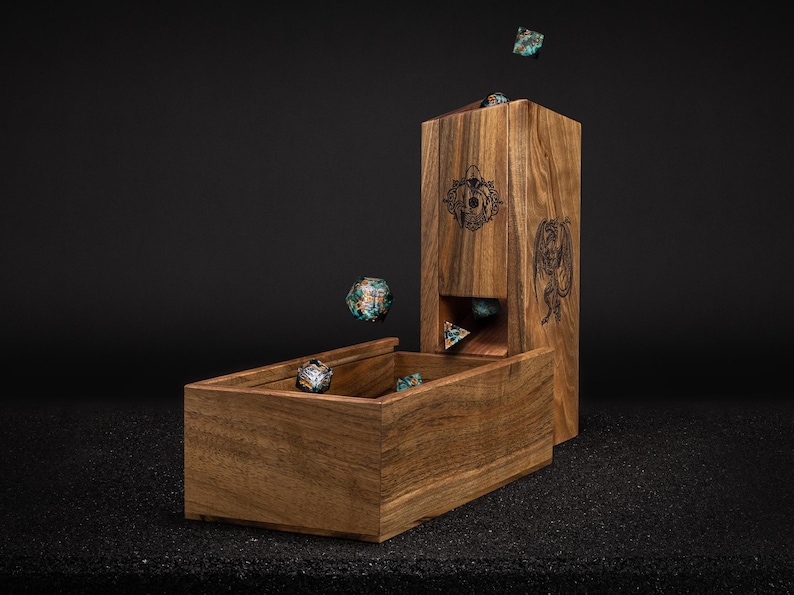 May include: A wooden dice tower and tray set. The tower has engraved designs and a slot for dice to roll into the tray. Several colorful dice are in the air and in the tray. The set is made of a warm-toned wood.