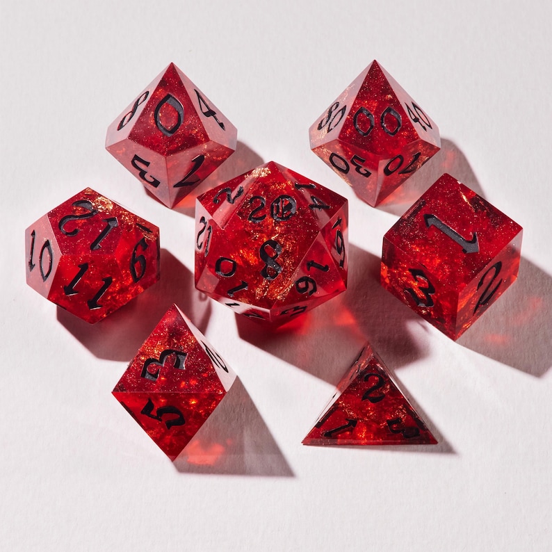 May include: A collection of seven red polyhedral dice with gold flecks and black numbering. The set includes a d20, d12, d10, d8, d6, and d4. These dice are designed for tabletop role-playing games and other dice-based games.