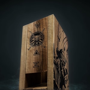 May include: Wooden box featuring engraved Witcher symbols and a detailed illustration of a figure. The box is made of light brown wood and has a hinged lid. The Witcher medallion and other symbols are etched on the front.